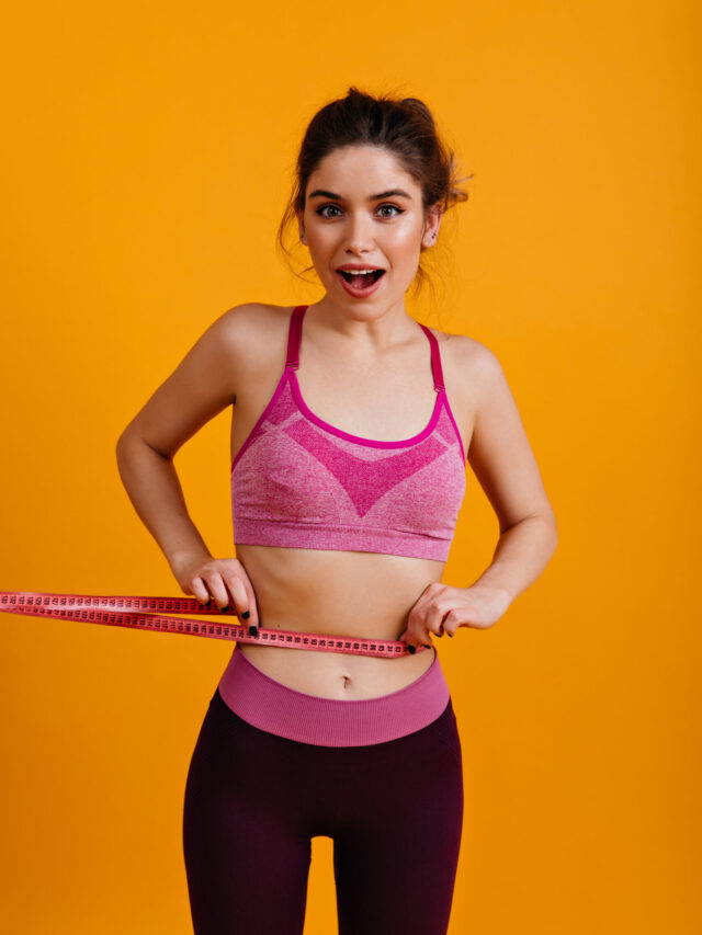 White young woman measuring her waiste. Lovely girl in sportswear holding measure tape